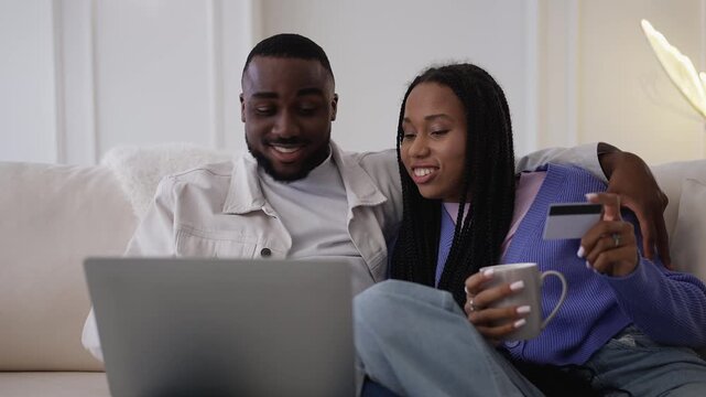 Happy Black couple enter credit card details on laptop while shopping online