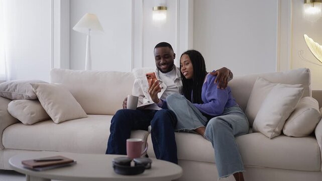 Happy young Black couple choose clothing on phone while shopping online together