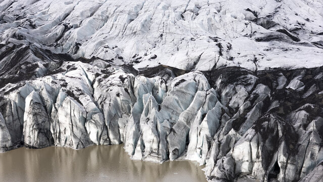 Aerial view of glacier patterns featuring deep crevasses, dark volcanic ash, and glacial meltwater in Kirkjubaejarklaustur, Skaftarhreppur, Iceland.