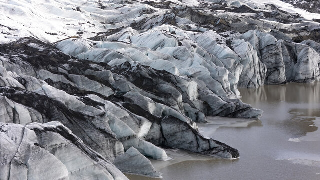 Aerial view of the intricate ice patterns and dark volcanic ash streaks of the glacier meeting a glacial lake in Kirkjubaejarklaustur, Skaftarhreppur, Iceland.