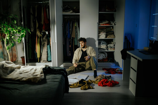 Overwhelmed youth stares blankly sitting on floor with alcohol drink. Severe isolation ruin