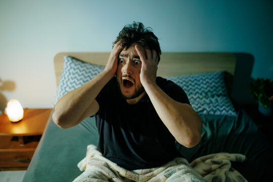 Desperate man holds head in terror during dark night battling severe insomnia and panic attacks