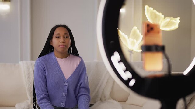 Young African American woman records video blog on phone, talking to followers