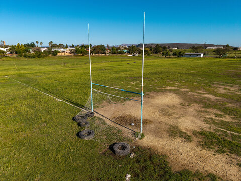 Aerial view of a rural rugby field with weathered goalposts, worn grass, and old tires at the base in Ladismith, Western Cape, South Africa.
