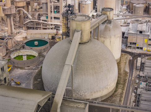 Aerial view of a massive dome storage structure, silos, and processing equipment inside a large cement manufacturing facility France.