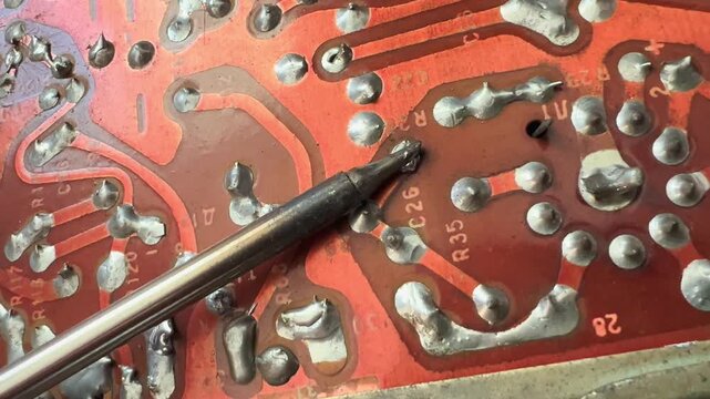 Soldering tool touches molten metal joints on a retro red printed circuit board