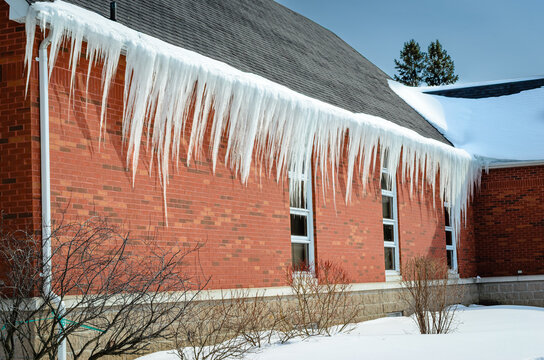 Long white icicles hanging from a black roof edge on a red brick walled building