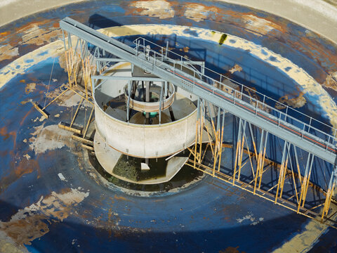 Aerial view of a circular water treatment clarifier with industrial metal structures and weathered blue basin surfaces in the United Kingdom.