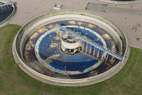 Aerial view of a circular water treatment clarifier tank with a central rotating mechanism and blue water, surrounded by grass in the United Kingdom.