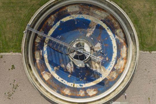 Aerial view of a circular water treatment clarifier tank with a central rotating bridge mechanism and weathered blue surfaces in the United Kingdom.