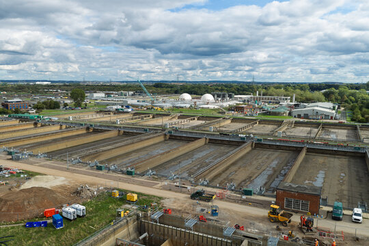 Aerial view of a water treatment plant featuring large rectangular sedimentation tanks, industrial infrastructure, and surrounding green fields under a cloudy sky in the United Kingdom.