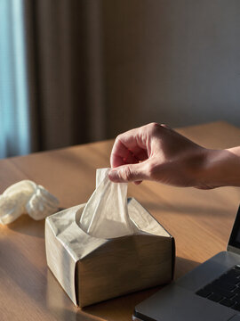 Hand pulls tissue beside laptop during seasonal cold at home desk