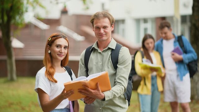 Two cheerful students posing with a book on university campus
