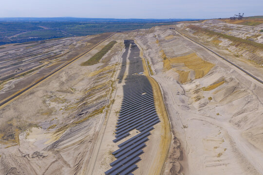 Aerial view of a large solar farm installed within the Hambach open-pit coal mine, featuring rows of solar panels on excavated sandy ground in Germany.