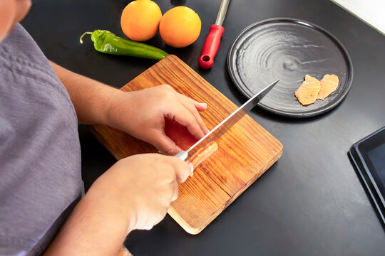 High angle view of chef hands slicing raw salmon on wooden board
