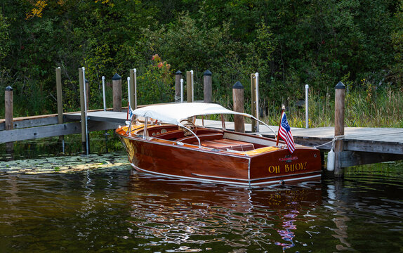 NISSWA, MN - 12 SEP 2024: Century wooden speedboat Oh Buoy with white canvas bimini, dark mahogany hull, docked near lily pads and forest, Nisswa, Minnesota.