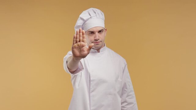 Serious professional male chef raises his hand in clear stop gesture toward the camera. Warning, prohibition, safety, rules and food control