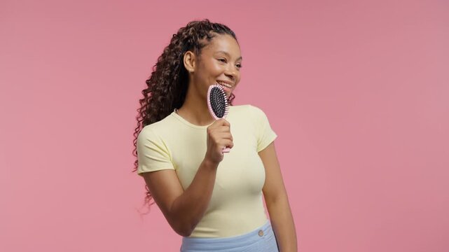 Playful Teenage girl Singing, Dancing With Hairbrush Instead Microphone On Pink Studio.Young woman having fun, listening to music, karaoke