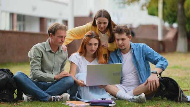 University students collaborating on laptop outside on campus lawn
