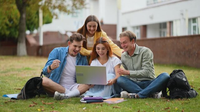 Excited university students celebrating success with laptop on campus lawn