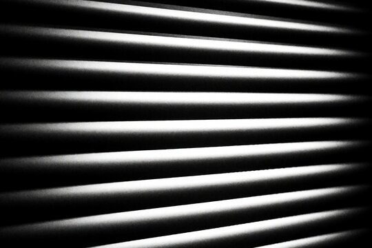 Abstract black, white background featuring horizontal window blinds. High contrast light, shadow create geometric pattern with parallel lines. Minimalist texture shows repetitive stripes, dark