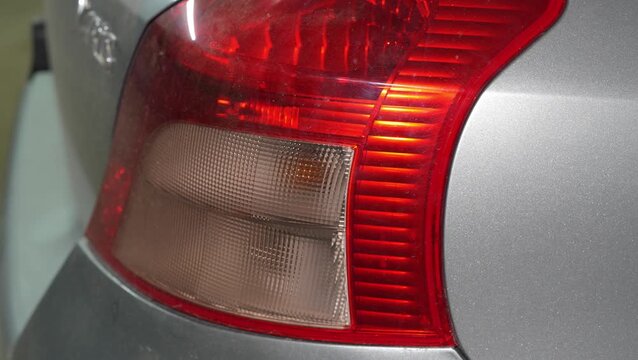 Close-up of red illuminated car taillight with amber section on silver vehicle