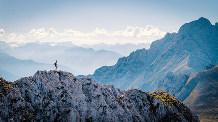 Hiker standing on a rocky summit during a via ferrata in the Austrian Alps near Innsbruck, Tyrol, with dramatic mountain peaks and a vast alpine landscape in the background. © Jag_cz