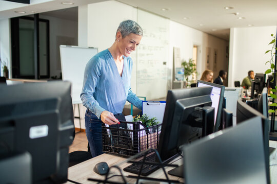 Smiling woman unpacks moving crate at office desk