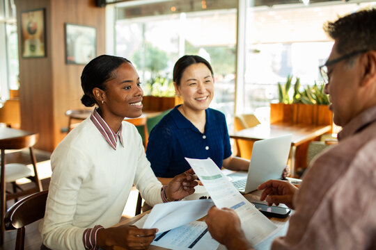 Three colleagues reviewing documents in a cafe