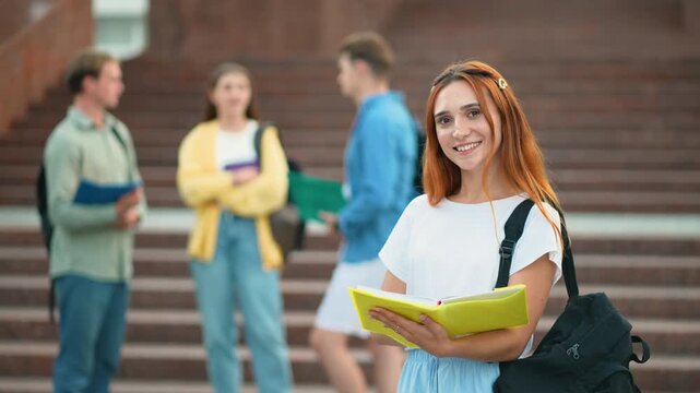 Young female student holding a book and smiling at the camera