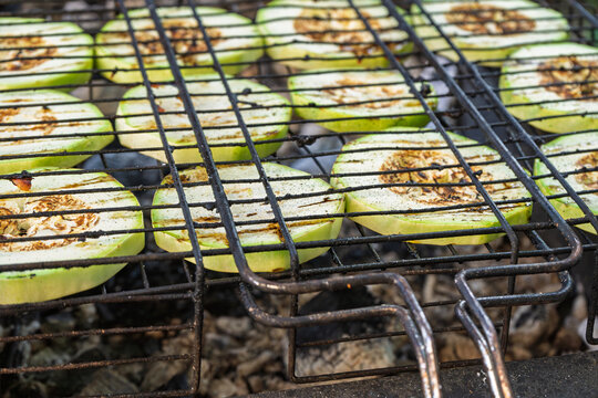 Grilled zucchini slices with browned marks cooking over charcoal
