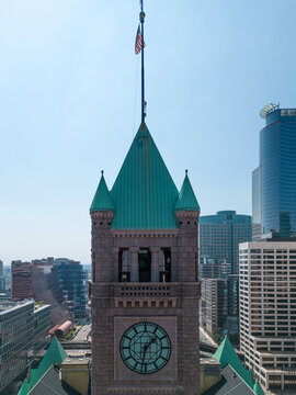 Aerial view of the historic Minneapolis City Hall clock tower with its distinctive green copper roof and clock face, rising above the modern skyline of Minneapolis, Minnesota, United States.