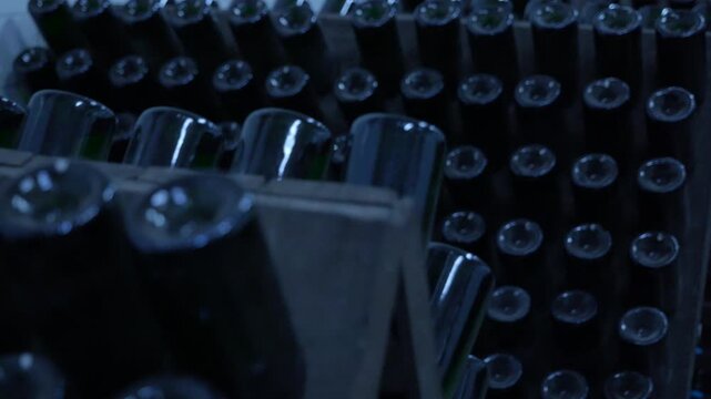 Wine bottles aging. Countless bottles of wine stored on wooden racks during the aging and fermentation process inside a dark, cool underground cellar, for producing high-quality sparkling wine