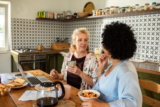 Two mature women talking over breakfast in kitchen