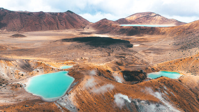 Aerial view of Tongariro Alpine Crossing featuring vibrant emerald volcanic lakes, rugged crater terrain, and steaming geothermal vents in Manawatu-Whanganui, New Zealand.