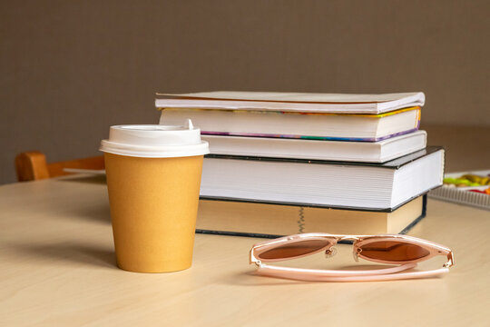Takeaway coffee cup beside stacked books and sunglasses on a table. Study break and reading. Education, student life and learning. Coffee break, work and relaxation.