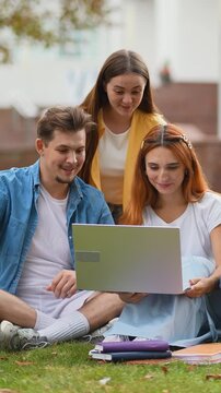University students studying together using laptop on campus lawn