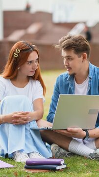 University students studying together using laptop on campus lawn