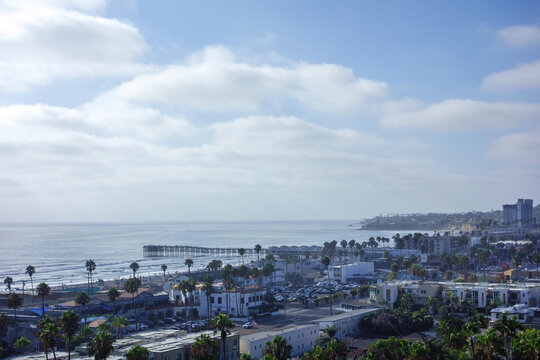 Crystal Pier stretching into the Pacific Ocean with the coastal town of San Diego under a cloudy sky, California in summer; back lit shot