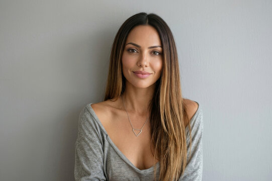 Portrait of a beautiful woman with long brown hair wearing a grey top and necklace against a grey background[cite: 14].