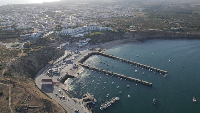Aerial view of the harbor in Sagres with fishing boats moored at the piers, surrounded by coastal cliffs and the town of Sagres, Sagres, Faro, Portugal.
