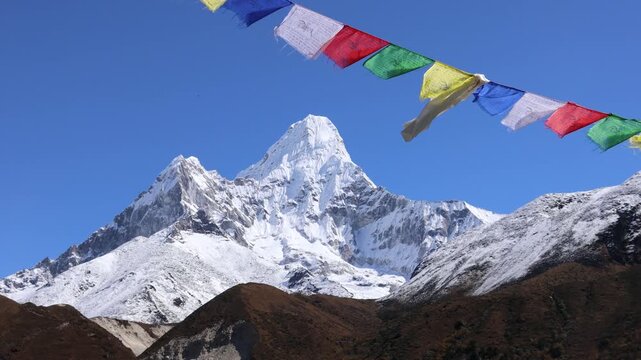 Colorful Buddhist prayer flags flutter in the Himalayan breeze with majestic Ama Dablam rising in the background. Vibrant fabric banners contrast beautifully against snow-covered peaks