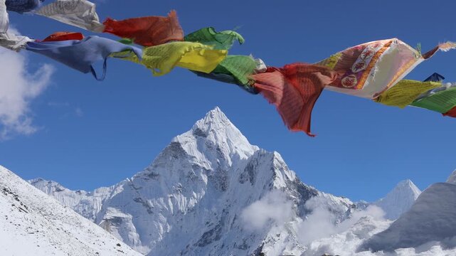 Colorful Buddhist prayer flags flutter in the Himalayan breeze with majestic Ama Dablam rising in the background. Vibrant fabric banners contrast beautifully against snow-covered peaks