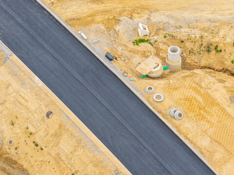 Aerial view of a road construction site with fresh asphalt, concrete curbs, and drainage pipes in Kartuzy, Pomeranian Voivodeshi, Poland.