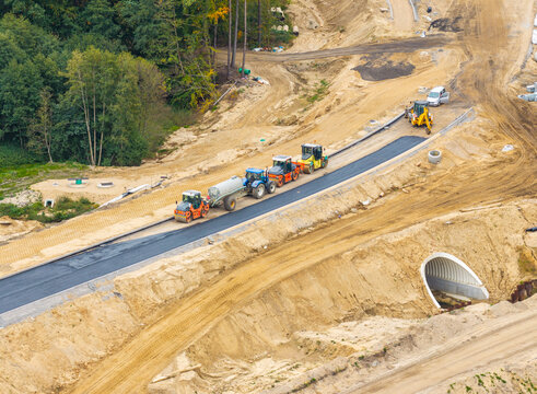 Aerial view of a road construction site with heavy machinery, including rollers and a tractor, working on a new asphalt road section in Kartuzy, Pomeranian Voivodeship, Poland.