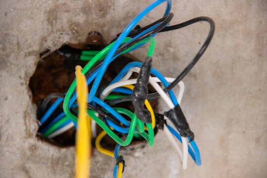 Colored electrical wiring with splices coming out of a concrete ceiling junction box. Focus on electrical installations, renovation, building maintenance, and civil engineering.