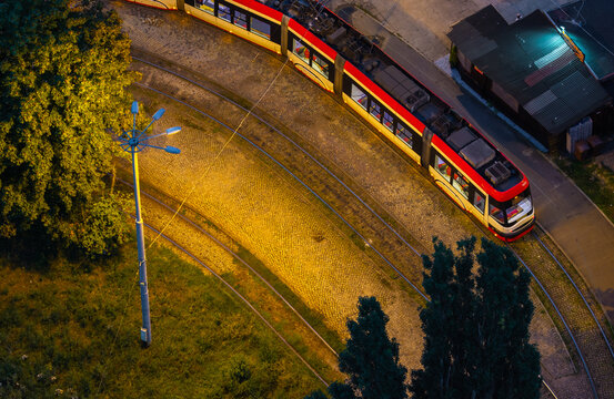 Aerial view of a modern tram traveling on cobblestone tracks at night, illuminated by street lighting in the Oliwa district of Gdansk, Pomeranian Voivodeship, Poland.