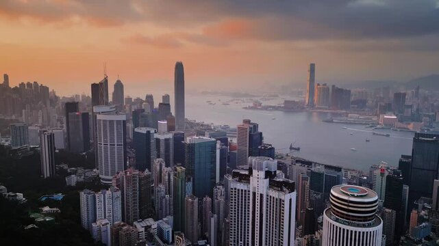 Sunrise hong kong skyline over kowloon waterfront in drone perspective reveals dense skyscrapers. Golden light on glass facade of towering buildings and harbor vessels moving slowly in calm atmosphere