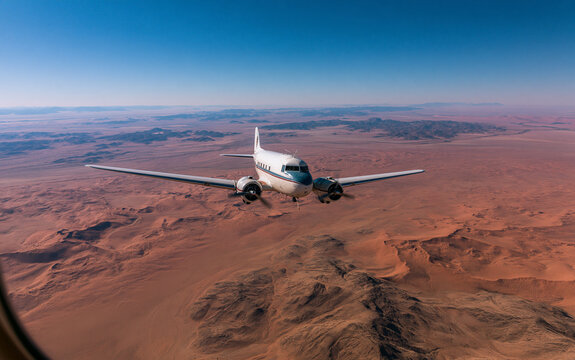 A twin-engine vintage propeller plane flies over the Namib Desert - Typical landscape of Namibia between Kalahari and Namib desert