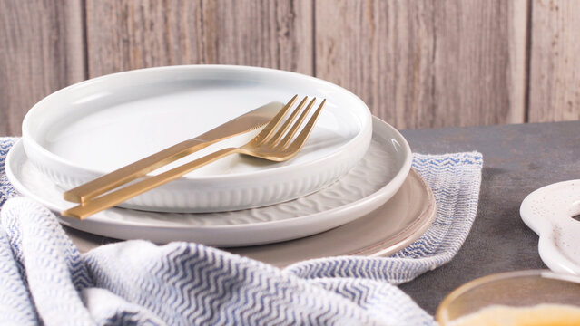 Elegant white ceramic tableware set with gold cutlery on a kitchen countertop